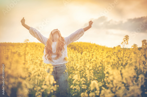 Happy smiling woman in yellow rapeseed field at sunset freedom concept