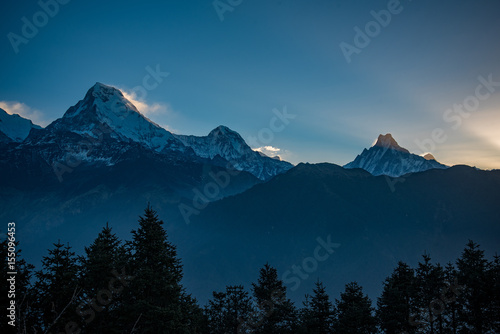 poonhill Winter sunset over snow-capped mountains with a view of the alpine valley and forest in the distance