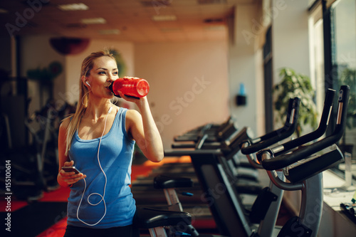 Beautiful young woman resting and drinking water in the gym