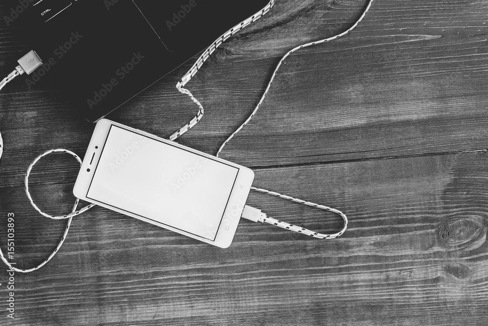 Workspace with laptop and charging blank smartphone on wooden desk Workspace with laptop and charging blank smartphone on wooden desk