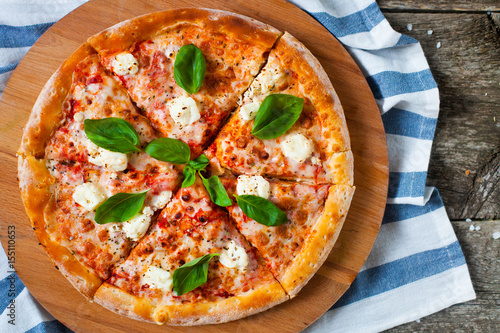 Homemade Pizza with tomato sauce, artichoke hearts, olives, Parmacotto, fresh mozzarella, parmesan and basil on the grey wooden background photo