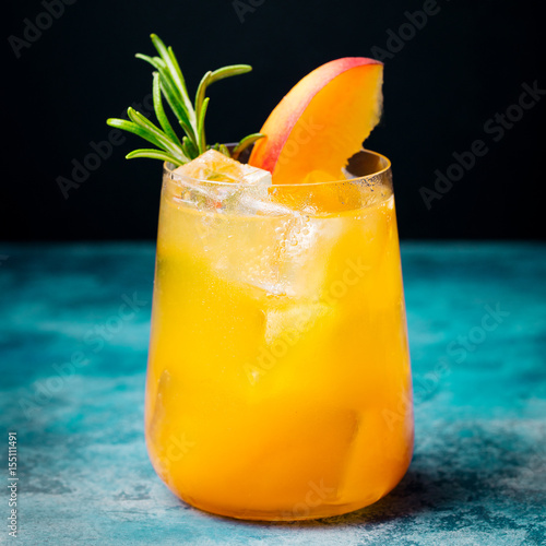 Peach cocktail, fizz with rosemary on blue stone background.