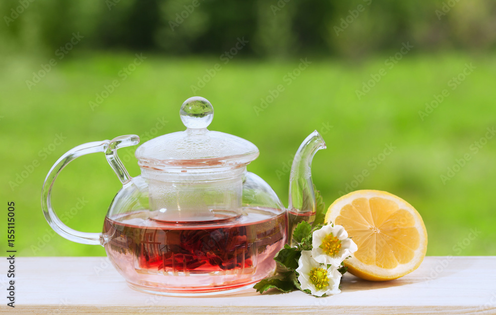 Teapot with fragrant herbal tea on a background of nature lemon and strawberry flower Teapot with fragrant herbal tea on a background of nature lemon and strawberry flower
