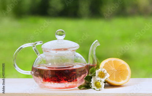 Teapot with fragrant herbal tea on a background of nature lemon and strawberry flower
