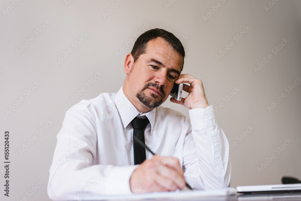 Businessman talking on phone with client, checking agenda Businessman talking on phone with client, checking agenda