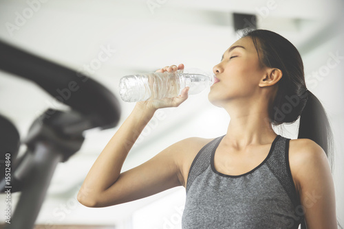 Asian woman in sportswear drinking water after workout at the gym.