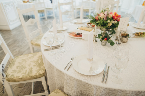 On the festive table in the wedding banquet area there are compositions of flowers, candles, plates, cutlery, napkins