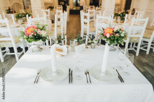 On the festive table in the wedding banquet area there are compositions of flowers, candles, plates, cutlery, napkins © AlexGukalovUkraine