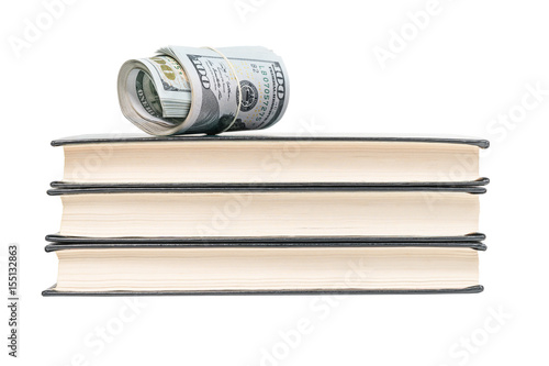 Money rolled into a tube and strapped a rubber band lying on top of a stack of three books