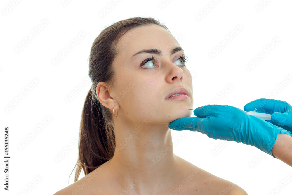 Portrait of a charming young girl who looks toward and beautician in blue gloves touches her face