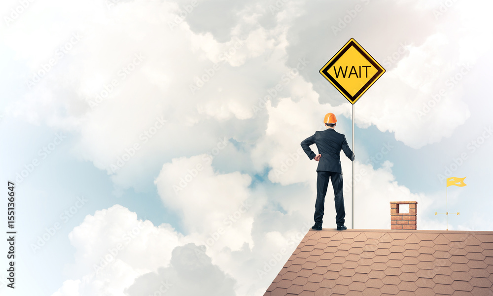 Young businessman on house brick roof holding yellow signboard. Young businessman on house brick roof holding yellow signboard.