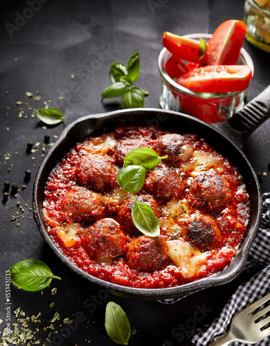 Meatballs in tomato sauce with addition cheese and fresh basil on iron pan, black background