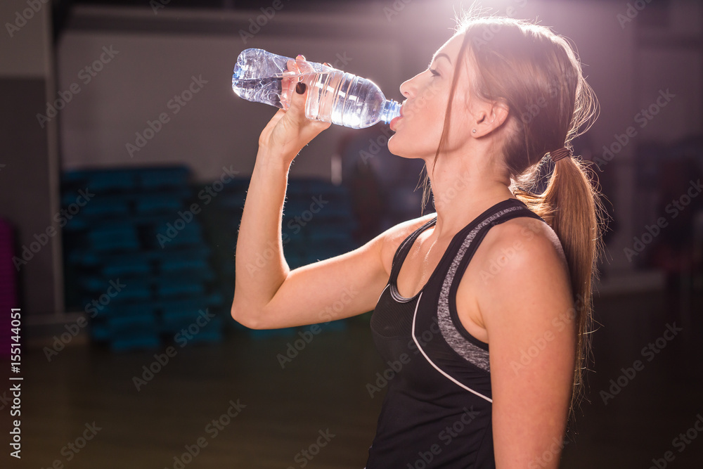 Fitness woman drinking water from bottle. Muscular young female at gym taking a break from workout. Fitness woman drinking water from bottle. Muscular young female at gym taking a break from workout.