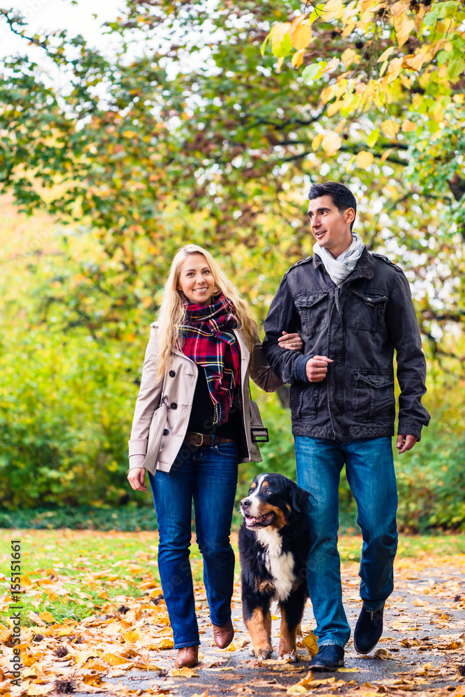 Woman and man with dog having autumn walk on a path covered with foliage