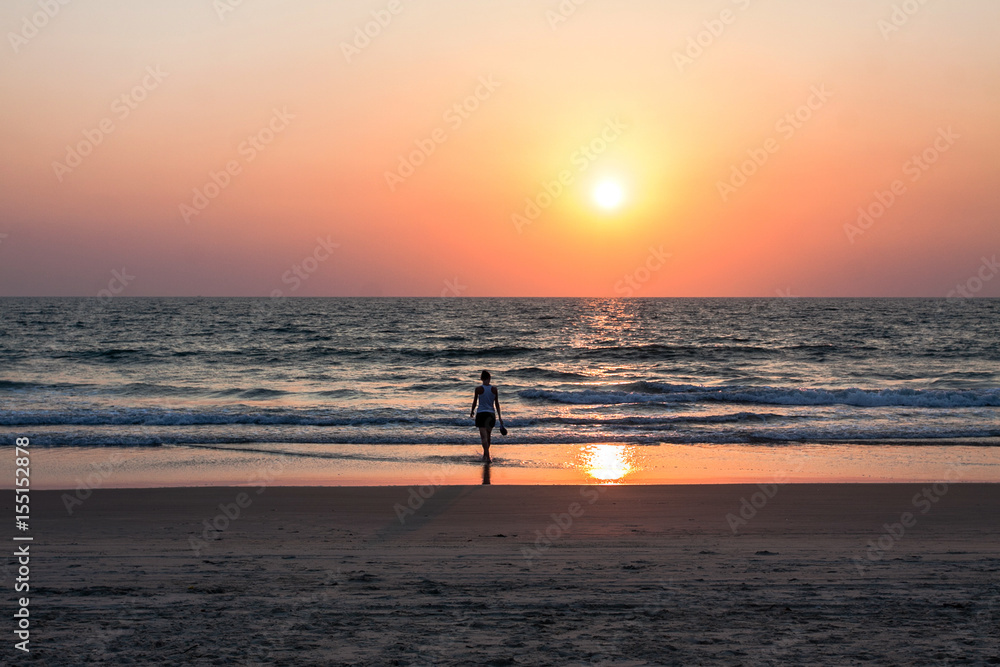 girl walking towards the ocean on a sand shore at sunset