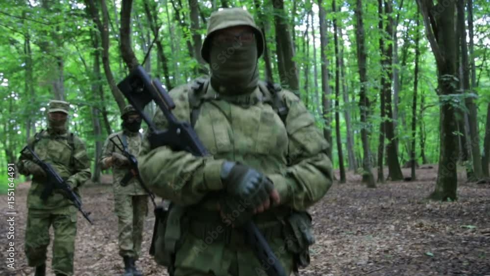 Guerilla warriors squad walking in one formation carrying their guns in the forest bushes. War battlefield maneuvers training. Steadicam shot. Guerilla warriors squad walking in one formation carrying their guns in the forest bushes. War battlefield maneuvers training. Steadicam shot.