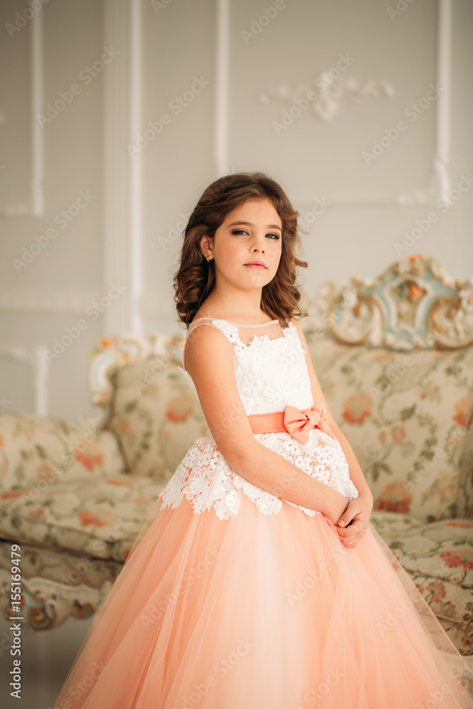 Little beautiful girl with brown hair in a Peach-colored dress. Poses for a photographer Little beautiful girl with brown hair in a Peach-colored dress. Poses for a photographer
