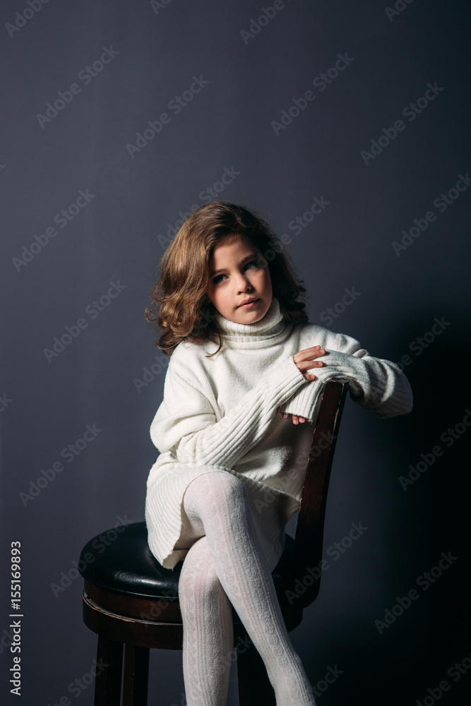 Little beautiful girl with brown hair in a light sweater and with a skirt of tulle.Studio. A princess poses for a photographer.