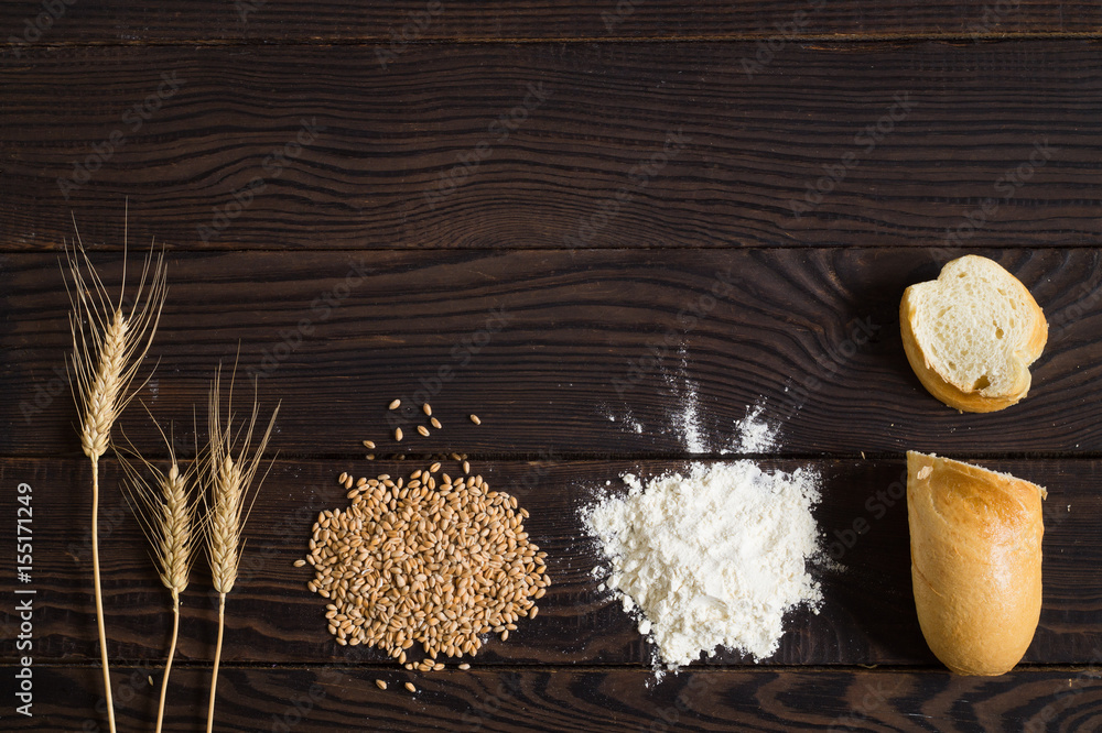 Wheat ears, grains, flour and sliced bread on a dark wooden table Wheat ears, grains, flour and sliced bread on a dark wooden table