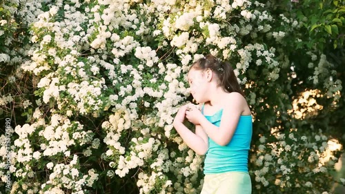 Cute little girl sniffing flowers and playing in the park in summer day.