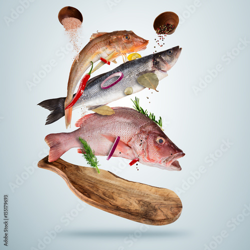 Fototapete Fresh sea fish with falling spices, flying above wooden board