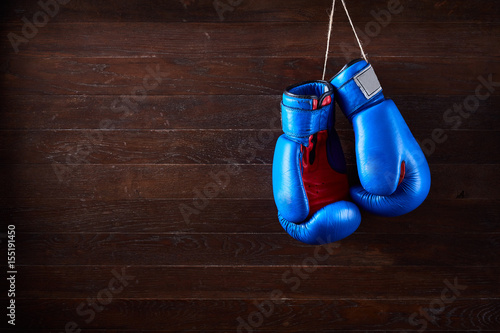A pair of bright blue and red boxing gloves hangs against wooden background. © Aleksey