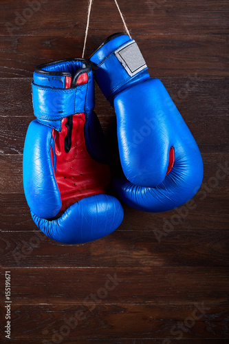 Blue and red boxing gloves hanging on wooden wall. © Aleksey