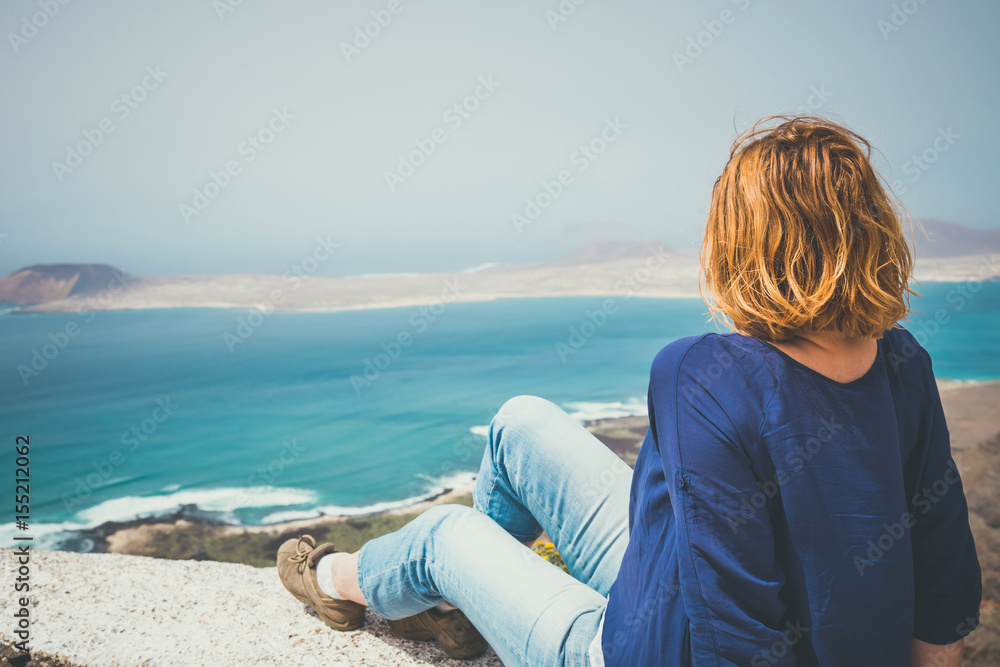 Young woman sitting on stone fence looking at sea