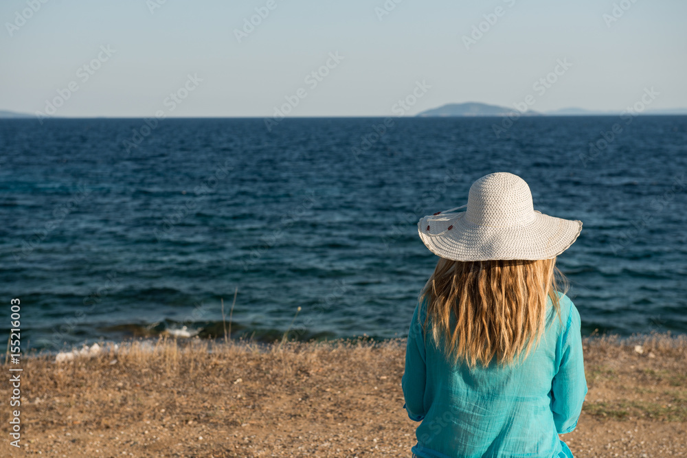 Young woman with hat sitting on beach with her back and space for text