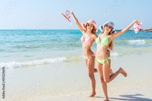 Happy bikini two asian women jumping of joy and success on perfect white sand beach on caribbean tropical vacation. Holiday girls with sexy slim suntan body running of freedom and happiness.