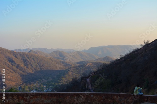 Hills around the amber fort and a man sitting on the wall of the fort in Jaipur, India