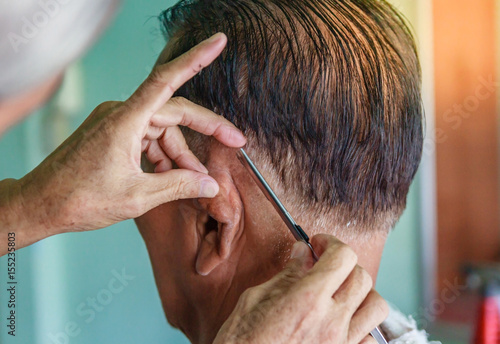 Master cuts hair and beard of men in the barbershop, hairdresser makes hairstyle for a senior asian man