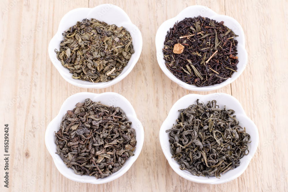 Green and black tea leaves in ceramic bowl on wood background Green and black tea leaves in ceramic bowl on wood background