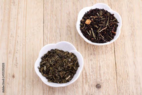 Green and black tea leaves in ceramic bowl on wood background