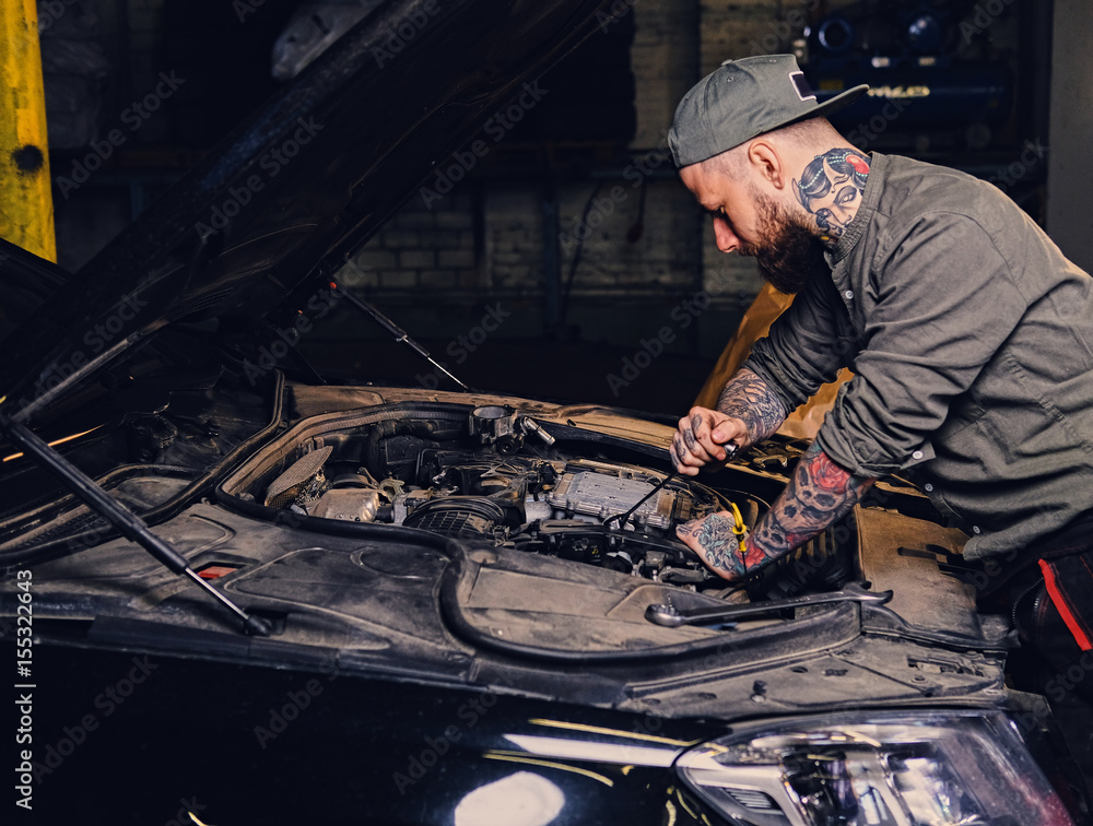 Bearded tattooed mechanics near car in a garage. Bearded tattooed mechanics near car in a garage.