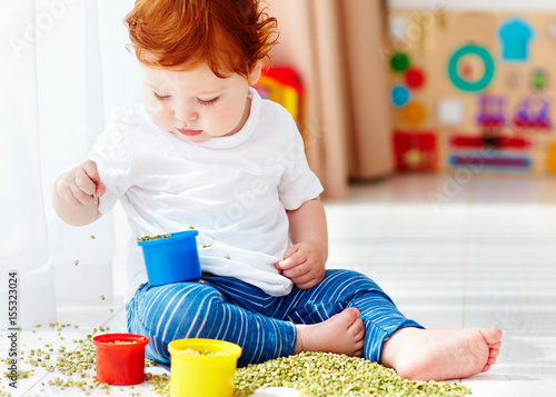 cute redhead baby boy developing his fine motility skills by playing with green peas at home