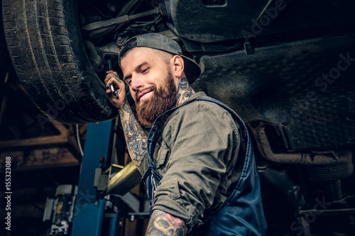 Bearded  mechanic working with the car's chassis in a workshop.