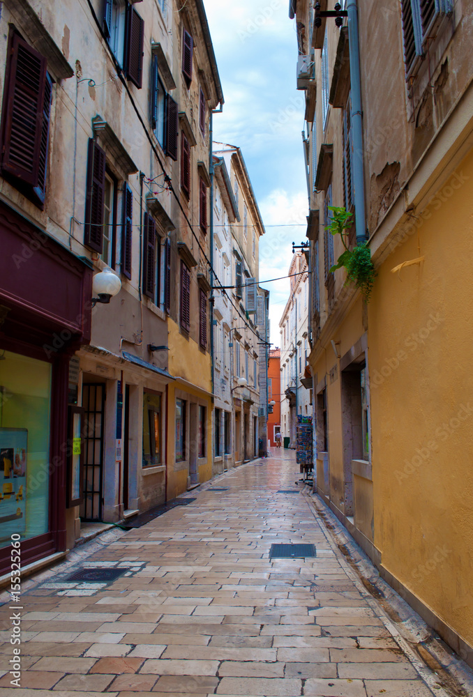 Cozy and empty narrow street between two stone houses with doors and shutters on a summer morning. Zadar center, Croatia