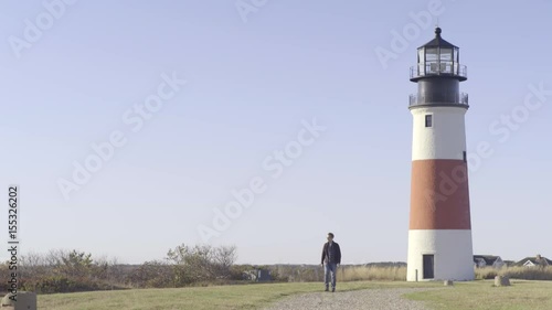 Man Walks Toward Camera, Away From Lighthouse  photo