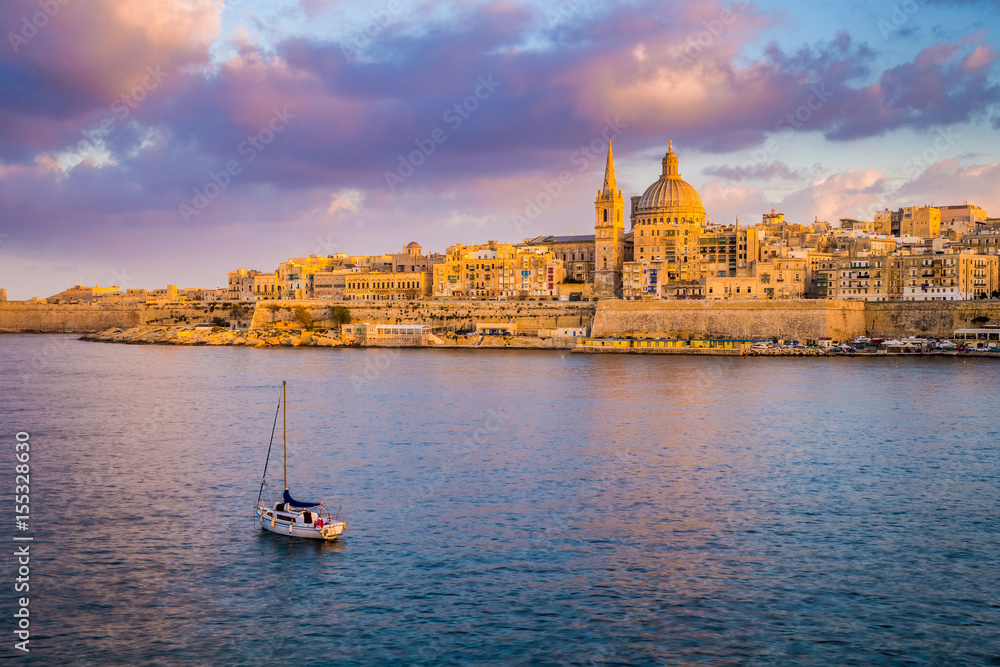 Fototapeta premium Valletta, Malta - St.Paul's Cathedral in golden hour at Malta's capital city Valletta with sailboat and beautiful colorful sky and clouds