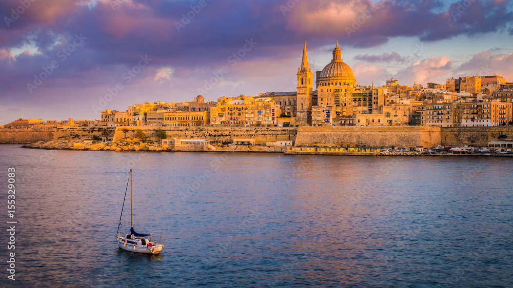 Valletta, Malta - St.Paul's Cathedral in golden hour at Malta's capital city Valletta with sailboat and beautiful colorful sky and clouds Valletta, Malta - St.Paul's Cathedral in golden hour at Malta's capital city Valletta with sailboat and beautiful colorful sky and clouds