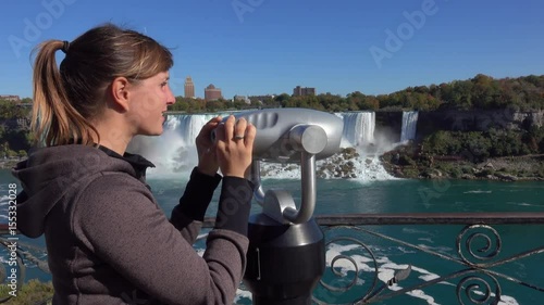Close up girl looking through the viewing binoculars on the balcony across the American and bridal veil falls crashing over rocky cliff