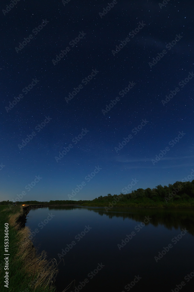 The stars in the night sky are reflected in the river. The landscape is photographed by moonlight. The stars in the night sky are reflected in the river. The landscape is photographed by moonlight.