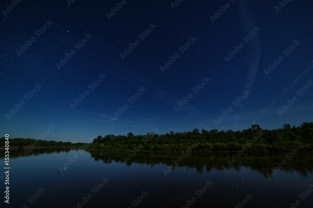 The stars in the night sky are reflected in the river. . The landscape is photographed by moonlight.