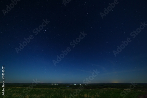 Stars in the night sky with city lights on the horizon. The landscape is photographed by moonlight. © olgapkurguzova