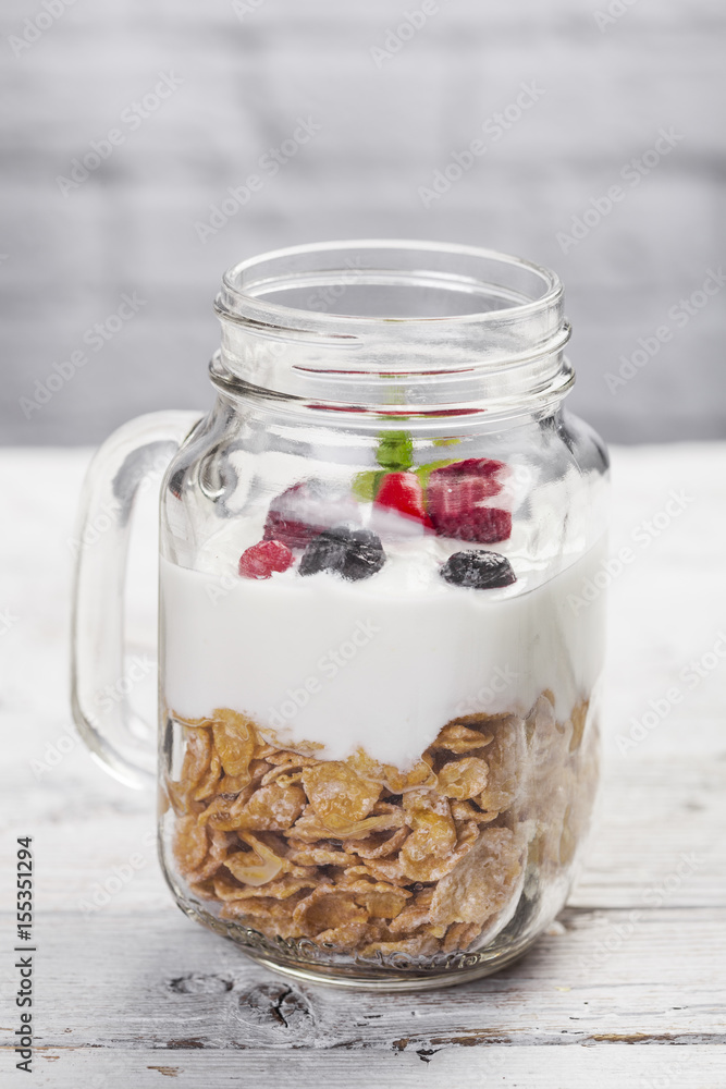 Cereals, yogurt and red fruits in a mason jar on a white wooden table Cereals, yogurt and red fruits in a mason jar on a white wooden table