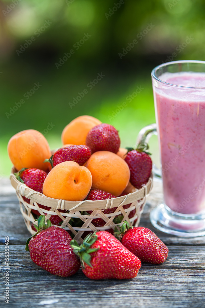 Wicker basket with strawberries and apricots, glass with strawberry smoothies, natural wood background Wicker basket with strawberries and apricots, glass with strawberry smoothies, natural wood background