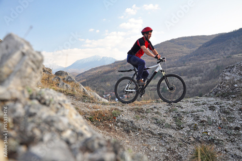 Young man riding a bike on hill under a mountain, extreme riding bicycle off road on rocks