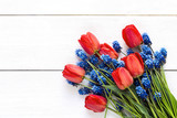 Bouquet of red tulips and blue muscaries flowers on white wooden background. Place for text.