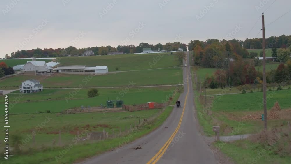 CLOSE UP: Traditional Amish family traveling in horse-drawn buggy through agricultural village past big dairy farm with large barn. Traditional Amish people breeding livestock for the milk production CLOSE UP: Traditional Amish family traveling in horse-drawn buggy through agricultural village past big dairy farm with large barn. Traditional Amish people breeding livestock for the milk production